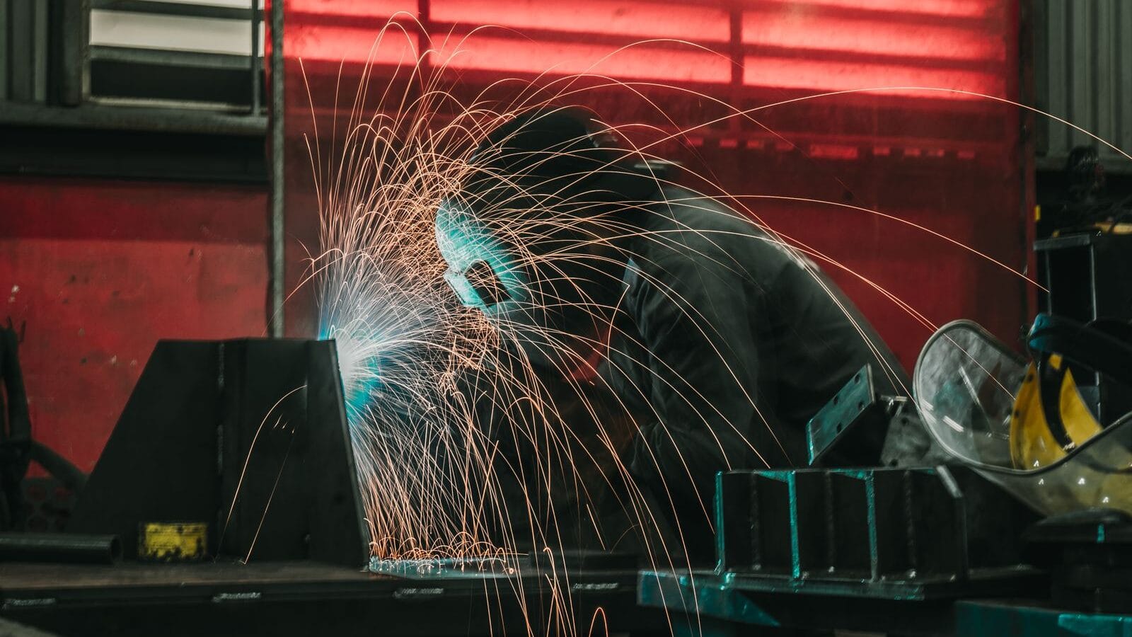 Welder in protective gear working with welding equipment in an industrial workshop