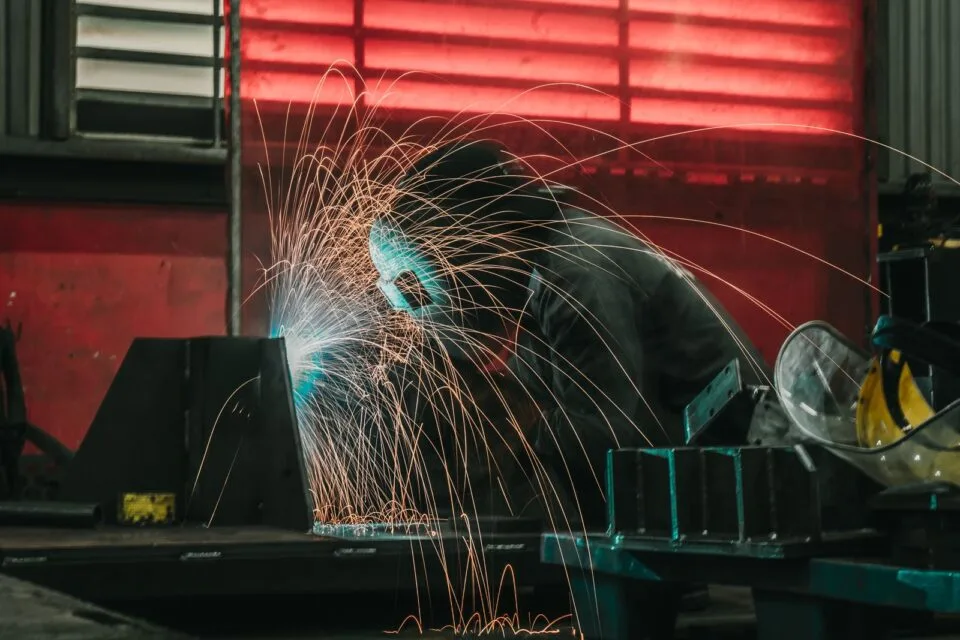 Welder in protective gear working with welding equipment in an industrial workshop