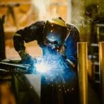 Professional welder in protective clothing working in an industrial fabrication workshop
