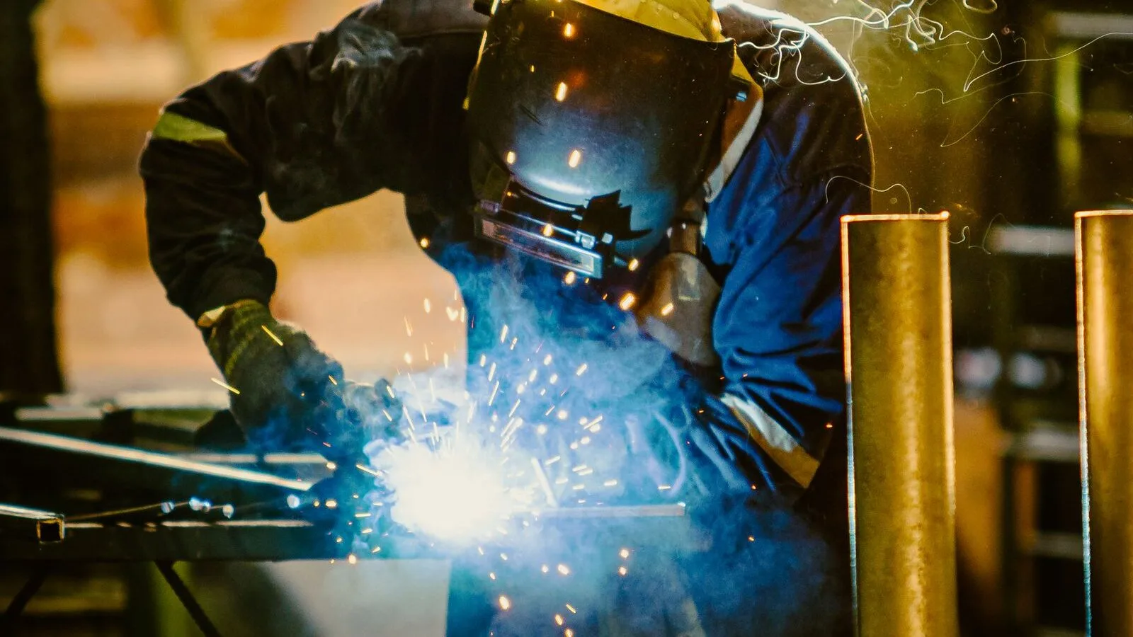 Professional welder in protective clothing working in an industrial fabrication workshop