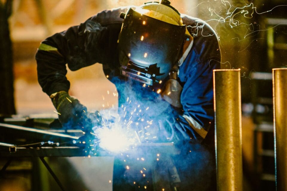 Professional welder in protective clothing working in an industrial fabrication workshop