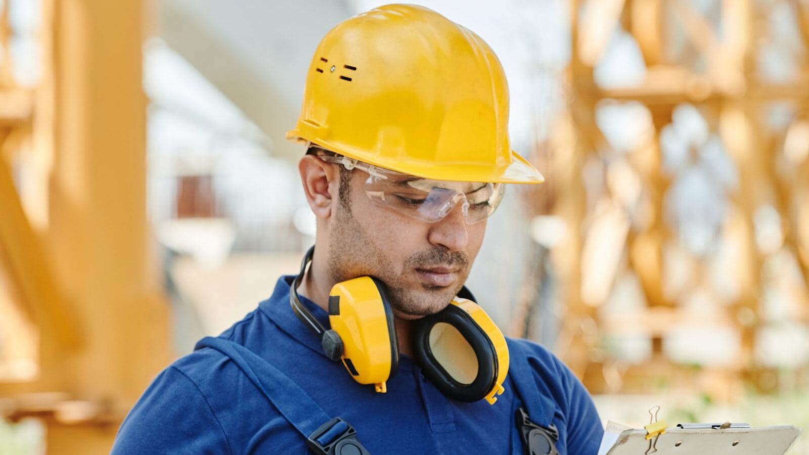 Engineer in hard hat and safety gear reviewing inspection documents on site
