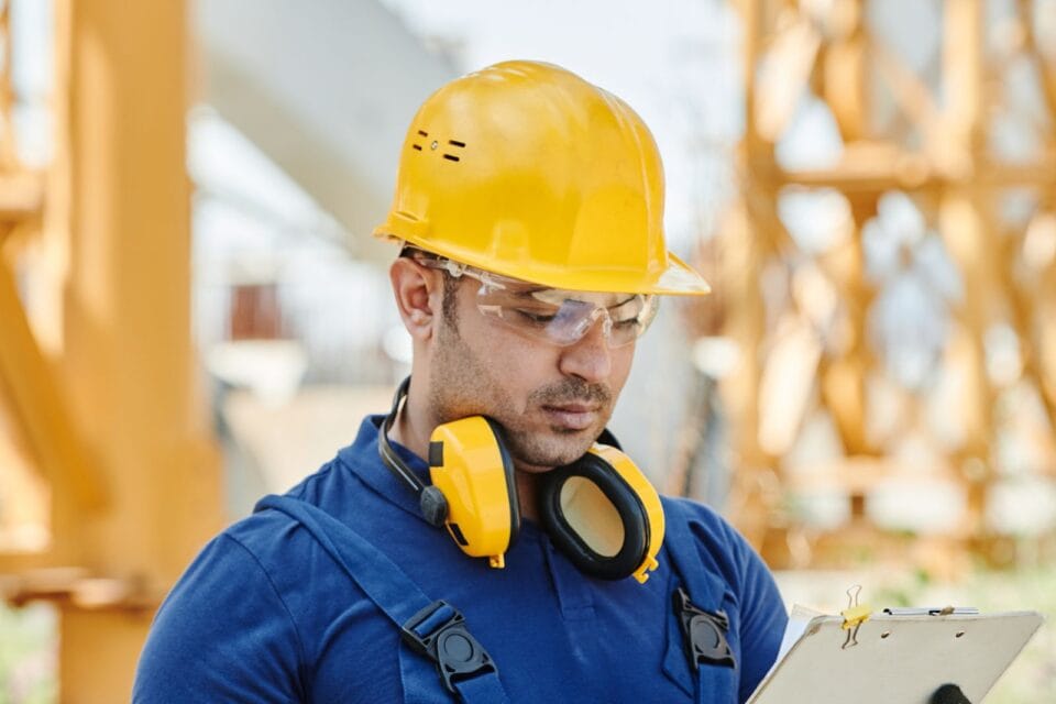 Engineer in hard hat and safety gear reviewing inspection documents on site