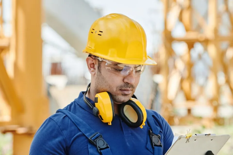 Engineer in hard hat and safety gear reviewing inspection documents on site