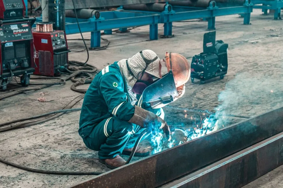 Welder in protective gear working on metal in a factory workshop