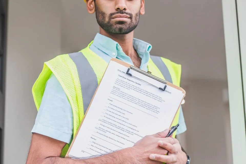 Engineer in hard hat and safety vest reviewing technical documents on a clipboard