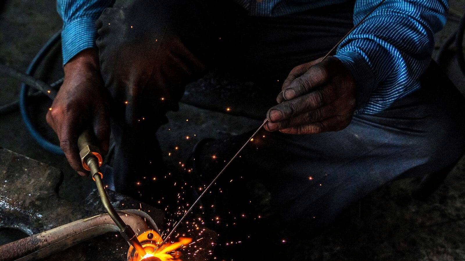 Close-up of a welder joining a steel pipe, sparks flying from the weld