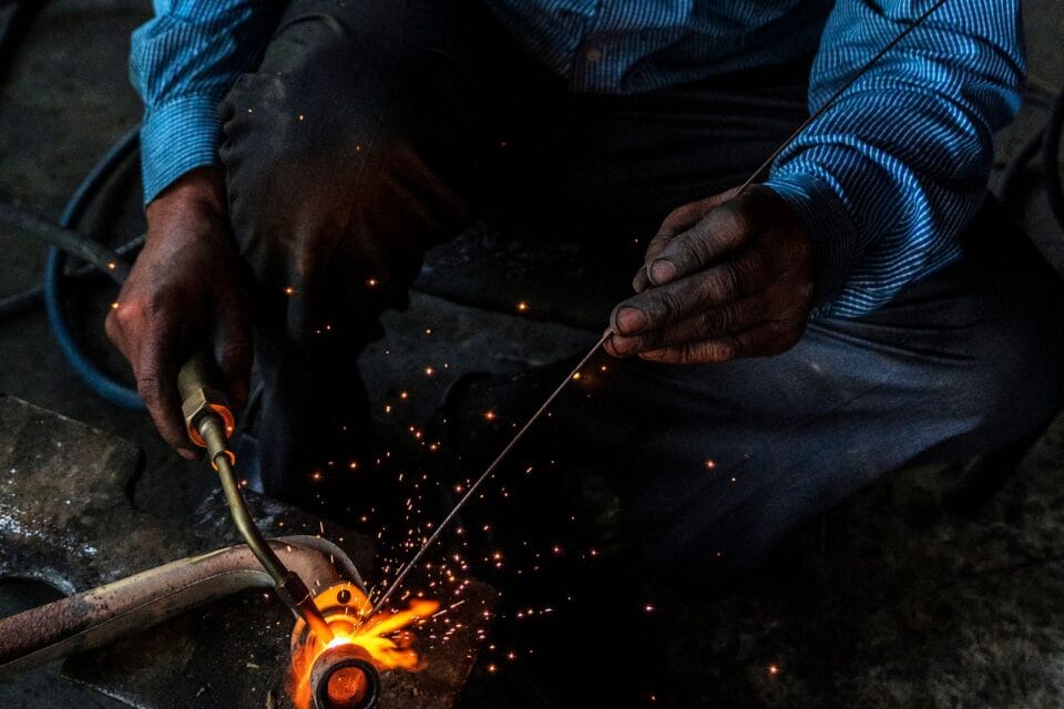 Close-up of a welder joining a steel pipe, sparks flying from the weld