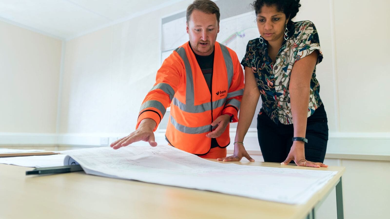 Two engineers in safety vests reviewing technical drawings together