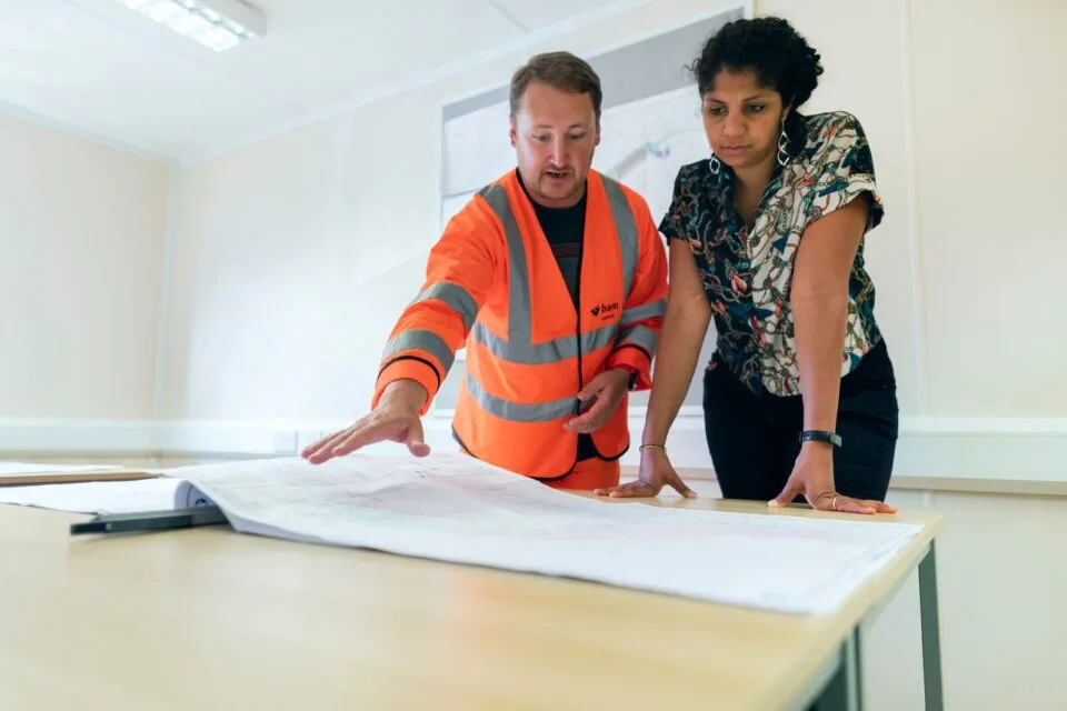 Two engineers in safety vests reviewing technical drawings together